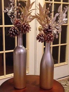 two silver vases sitting on top of a table filled with pine cones and flowers