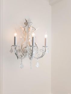 a chandelier hanging from the side of a white wall with two candles on it