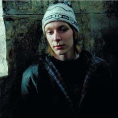 a young man wearing a knitted hat standing in front of a stone wall