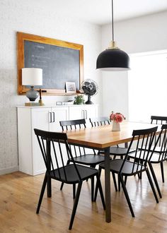 a dining room table with black chairs and a chalkboard on the wall behind it