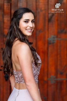 a beautiful young woman standing in front of a wooden wall wearing a dress and smiling