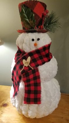 a snowman wearing a red and black plaid scarf with a hat on it's head