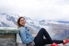 a woman sitting on top of a stone wall next to snow covered mountains