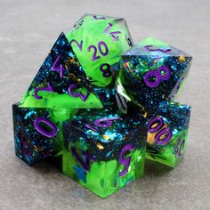 green and purple dices with numbers on them sitting on the floor in front of a gray background