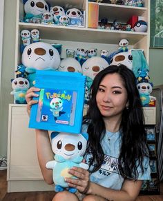 a woman holding up a stuffed animal in front of a book shelf