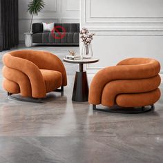 two orange chairs and a table in a room with white walls, flooring and furniture