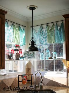 a kitchen sink sitting under a window covered in blue and green curtains