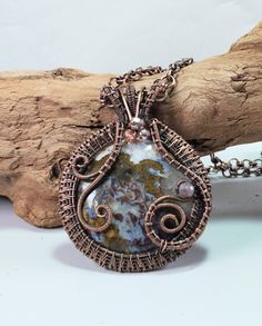 a wire wrapped pendant is sitting on a piece of driftwood next to a branch