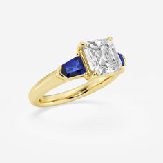 a yellow gold ring with an emerald and blue sapphire in the center, on a white background