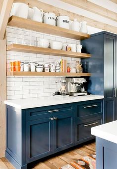 a kitchen with blue cabinets and white subway tile backsplash, wooden shelves above the sink