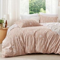 a bed with pink comforter and pillows in front of a window