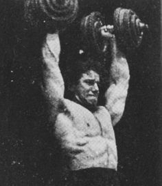 a man lifting two large dumbs in front of his head and chest, with one arm behind the other