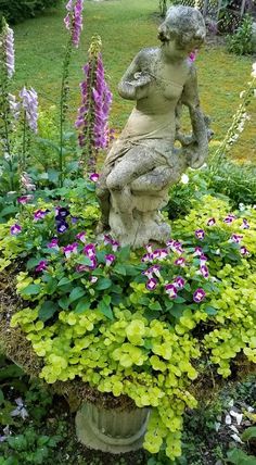 a statue sitting on top of a planter filled with purple and white flowers in a garden