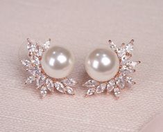 a pair of pearl and crystal earrings on a pink surface with white fabric in the background