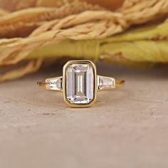 an emerald and diamond ring sits on a table next to dried yellow cornflowers