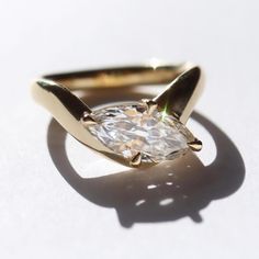 a gold ring with a white diamond in the center on a white surface, it appears to be casting a shadow