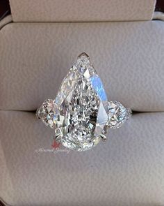 a fancy diamond ring sitting on top of a white cloth covered cushion in a box