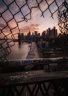 the sun is setting over a city skyline as seen through a chain link fence with graffiti on it