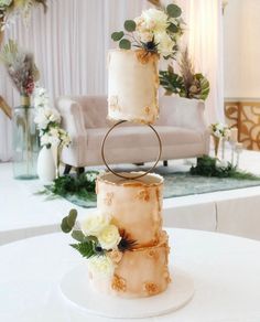 three tiered wedding cake with white flowers and greenery sitting on a round table