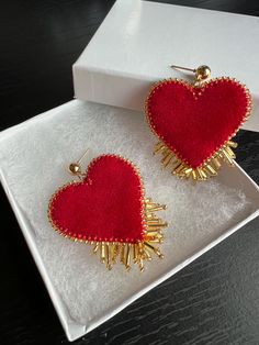 a pair of red heart shaped earrings sitting on top of a white box next to a black table