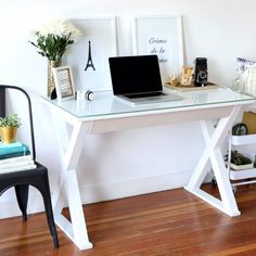 a laptop computer sitting on top of a white desk next to a black chair and potted plant