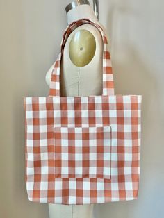 This large carryall tote is made from reclaimed fabric with a sturdy twill weave and an orange and cream gingham pattern. It features a roomy outer pocket, snap closure, and interior hook for your keys. This bag can easily hold a laptop, books, and other daily essentials. Perfect for a summer picnic or a fall day.  During the design process, clothing companies use and discard an enormous amount of fabric. I make my products using these pre-consumer materials. Your purchases give these fabrics new life and prevent them from being discarded and sent to a landfill. Thank you for your support! Measurements: 15"x17" Materials: Burn-tested mixed synthetic fabric. Fabric and hook are reclaimed materials, snap closure is new material. Carryall Tote, Gingham Pattern, Fall Day, Twill Weave, Summer Picnic, Daily Essentials, Synthetic Fabric, Autumn Day, Clothing Company