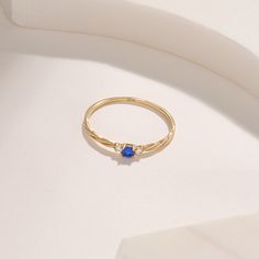 a gold ring with a blue stone sits on a white surface