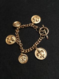 Beautiful and cute toggle bracelet that has Fleur de Lis charms and coin charms. This is very much a Y2K  jewelry. This is unsigned, but purchased at an estate auction.  Great condition.  SO pretty.  This is 7. Inches long. Vintage Gold-tone Jewelry With Logo Charm, Vintage Gold Bracelet With Logo Charm, Vintage Gold-tone Jewelry With Toggle Clasp, Vintage Gold Dangle Charm Bracelet, Vintage Gold-tone Metal Charm Bracelet, Gold-tone Metal Charm Bracelet With Vintage Charm, Vintage Adjustable Bracelet With Dangling Charms, Vintage Adjustable Bracelets With Dangling Charms, Adjustable Gold Charm Bracelet Collectible