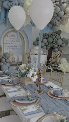 the table is set for a baby shower with blue and white decorations, balloons, and paper garlands