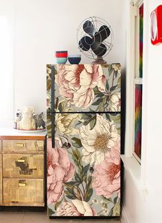 an old refrigerator with flowers painted on it in a room next to a dresser and fan