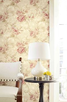 a living room with floral wallpaper and a chair next to a table that has a lamp on it