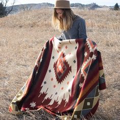 a woman sitting on the ground with a blanket in front of her and a hat over her head