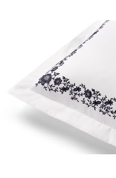 a white pillow with black embroidered flowers on the front and sides, sitting on a white surface