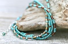 "This gorgeous silk cord beaded bracelet is made with a variety of turquoise blue and bronze beads. Wraps around the wrist 4x, clasp onto an adjustable sterling silver chain closure. Wear it alone for a minimalist look or layer with your favorites. Well made and beautiful! Fits wrist sizes: 6.5\"-7 1/4\" (adjustable) 100% natural silk cord Japanese glass beads Please note that pictures are deliberately taken to show detail and up close in my pieces. Therefore, be aware that some jewelry will loo Turquoise Multi-strand Bracelets With Tiny Beads, Turquoise Multi-strand Tiny Beads, Blue And Bronze, Multi Wrap Bracelet, Bracelet Layering, Beaded Wrap Bracelets, Silk Cord, Beaded Wraps, Bracelet Beaded