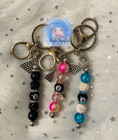 three key chains with charms attached to them sitting on a bed covered in stars and sparkles