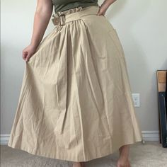 A Classic Belted Skirt With A Fun Asymmetrical Twist. It Has A Roomy Pocket On One Side, And A Gathered Elastic Waistband That Allows It To Fit A Range Of Sizes Casual Solid Color Belted Skirt, High-waist Beige Cotton Skirt, High Waist Beige Cotton Skirt, Solid Pleated Asymmetrical Skirt, Casual Asymmetrical Maxi Skirt With Gathered Detail, High Waist Cotton Gathered Maxi Skirt, Spring Belted Wrap Skirt In Relaxed Fit, Casual Asymmetrical Pleated Skirt For Spring, Casual Asymmetrical Gathered Maxi Skirt