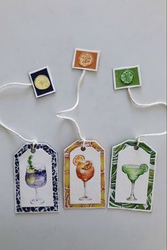 four tags with different types of drinks hanging from strings on a white surface, one has a gold medal and the other has an orange slice of lime