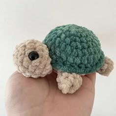 a hand holding a small crocheted turtle on it's back and head