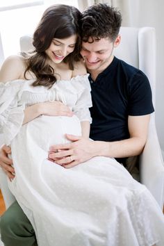 a pregnant couple cuddle while sitting on a couch