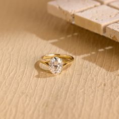 a yellow gold ring with a single diamond on the surface next to a brick wall