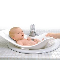 a baby sitting in a bathtub next to a faucet and soap dispenser