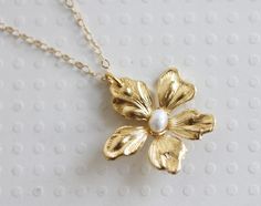 "This sweet little pendant necklace features a gold plated daisy flower hand wired wrapped with a creamy white fresh water pearl. Great gift for the flower lover in your life. Wonderful spring bridesmaid's necklace. Hangs from a fine 14 karat gold filled chain. Spring clasp closure The daisy is 1 \" wide ** The last photo show's a different pansy same size with a bird charm . Spring closure clasp Photoed with a 16\" chain on model H A N D M A D E * We hand make all pieces in our Water Mill New Y Gold Daisy Necklace, Flower Gold Necklace, Flower Pearl Necklace, Gold Flower Necklace, Daisy Jewelry, Bridesmaid Pearls, Water Mill, Daisy Necklace, Necklace Flower