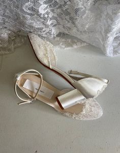 a pair of white shoes sitting on top of a bed next to a lace curtain