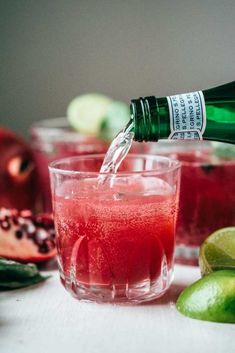 a bottle of water being poured into a glass filled with red liquid and limes