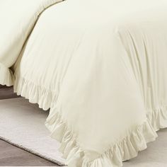 a bed with white sheets and ruffled bedspread on top of carpeted floor