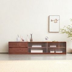 a living room with white walls and a wooden entertainment center on the floor next to a potted plant