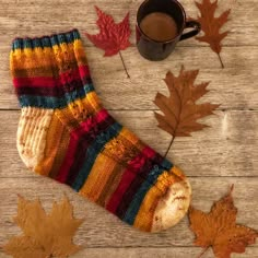 a cup of coffee and some leaves on a wooden table with a knitted sock