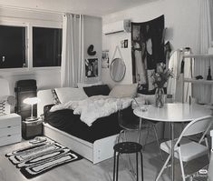 a black and white photo of a small living room with a couch, table, chairs, rugs and pictures on the wall