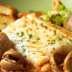 a close up of food on a plate with clams and bread in the background