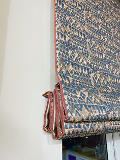 a blue and gold patterned curtain hanging from the side of a window with a red tie on it